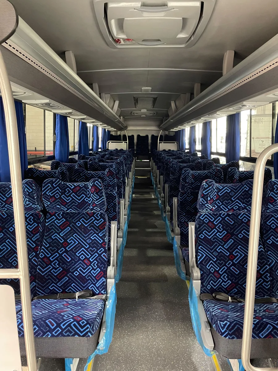 Interior de autobús con asientos reclinables de tela azul y cinturón de seguridad.