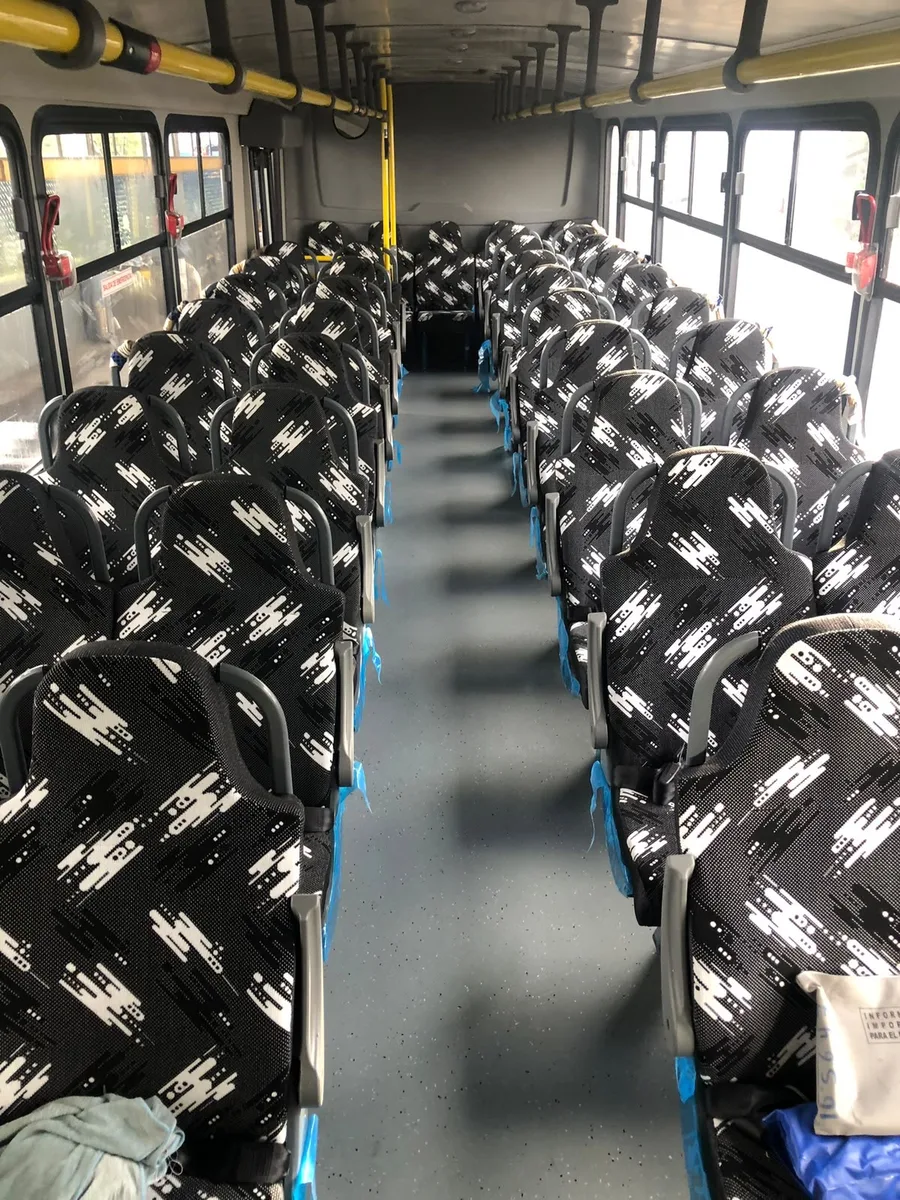 Interior de autobús con asientos altos tapizados en tela de patrón geométrico.
